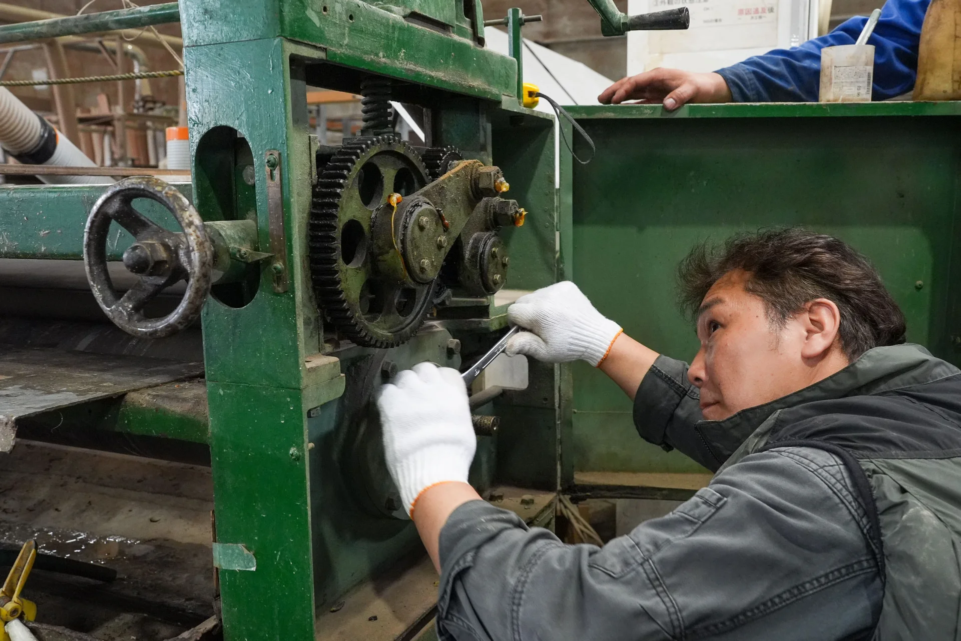 木工機械の駆動部を工具で調整する技術者